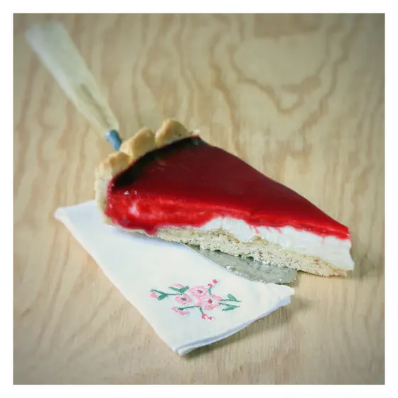 Ein Tortenstück mit roter Fruchtschicht auf einer bestickten Stoffserviette