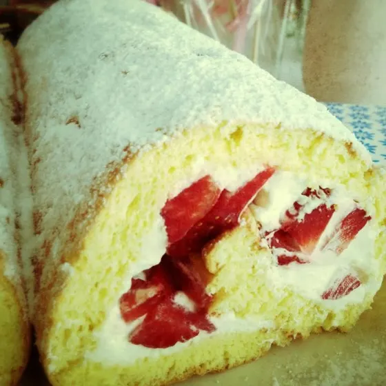 Eine angeschnittene Biskuitrolle mit Erdbeeren und Sahne