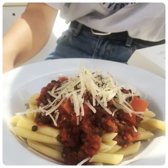 Ein Teller mit Nudeln, Tomatensauce und geriebenem Käse wird an den Tisch gebracht